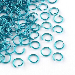 Peut inclure: Un grand nombre d'anneaux de saut en métal bleu turquoise. Les anneaux de saut sont petits et ronds, et ils sont dispersés sur un fond blanc.