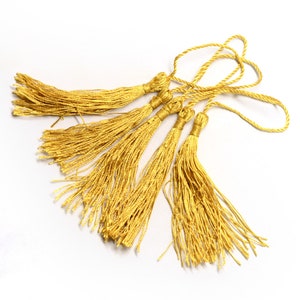 May include: Five gold tassel cords with loops at the top. The tassels are made of a soft, silky material and are approximately 5 cm long.
