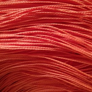 May include: Close-up of a vibrant orange rope, tightly coiled and layered. The texture of the rope is clearly visible, with individual strands twisted together. The color is consistent throughout, creating a warm, inviting visual.