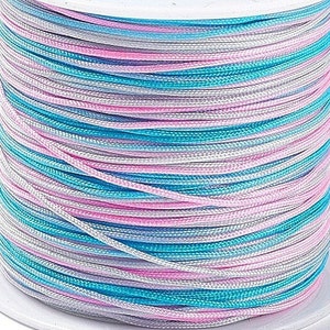 May include: A spool of multi-colored waxed cord. The cord is a mix of light blue, pink, and white.