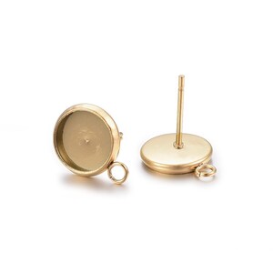 Peut inclure: Une paire de montures de boucles d'oreilles dorées avec une bélière ronde et une boucle pour attacher un charme. Les montures sont conçues pour tenir une pierre en cabochon.