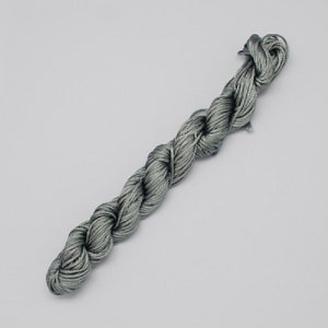 May include: A spool of silver gray waxed cord, a type of thread used for jewelry making and crafts.