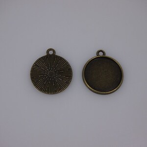 Op de afbeelding: Twee ronde metalen hanger-schalen met een bronzen afwerking. Een schaal heeft een getextureerd oppervlak en de andere is glad. Beide schalen hebben een lus aan de bovenkant om op te hangen.