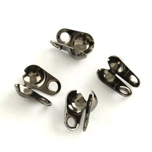 May include: Four black metal bead caps with a loop on each side. The caps are designed to be used to finish off the ends of a beaded necklace or bracelet.