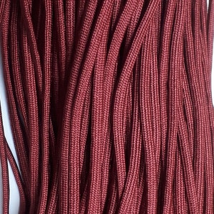 Può includere: Primo piano di un fascio di paracord marrone, un tipo di corda di nylon resistente.