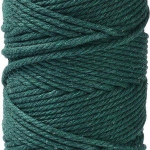 Può includere: Un rocchetto di cordoncino in cotone verde scuro. Il cordoncino è avvolto strettamente e ha un aspetto naturale e rustico.