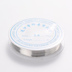 May include: A spool of silver-colored wire with a white label that reads "IMPORTED JEWELRY DEDICATED COPPER IMPORTED COPPER JEWELRY DEDICATED" and "Size 0.4 mm/m Longth m".