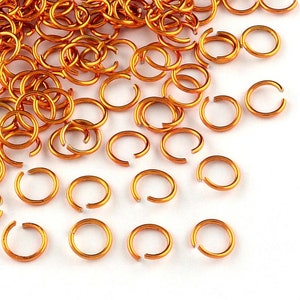 Op de afbeelding: Een stapel kleine, oranje metalen springringen. De ringen zijn verspreid over een wit oppervlak.