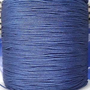Pode incluir: Um carretel de linha azul marinho. A linha é enrolada firmemente, criando uma superfície texturizada. A cor é um azul profundo e sólido, adequado para vários projetos de artesanato. A linha parece ser feita de um material durável.