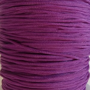 May include: A close-up of a spool of purple cord. The cord is tightly wound and has a smooth, shiny finish.
