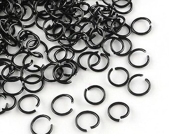 May include: A collection of small, black, open jump rings scattered on a white surface. The rings are made of metal and have a glossy finish. Some rings are connected, while others are separate.