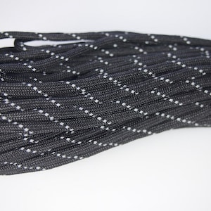 Könnte beinhalten: Schwarzes Paracord mit weißem reflektierendem Faden, der über die Länge des Seils verläuft.
