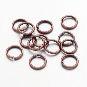 Op de afbeelding: Een groep van 12 antieke koperen sprongringen, elk met een diameter van ongeveer 1,2 cm. Deze ringen zijn perfect voor het maken van sieraden, knutselen en andere doe-het-zelfprojecten.