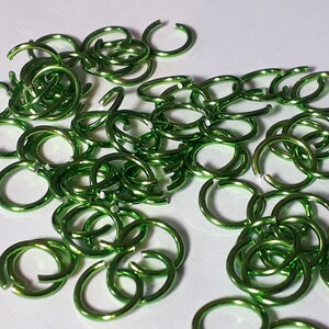 Könnte beinhalten: Ein Haufen kleiner, glänzender, grünfarbener Metall-Sprünge. Die Ringe sind klein und haben eine glänzende Oberfläche.