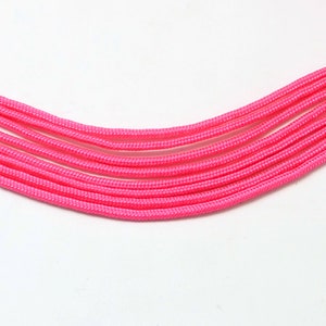 Peut inclure: Gros plan sur du paracord rose, un type de cordon en nylon résistant, disposé en forme de courbe. Le cordon est lisse et a une finition légèrement brillante.