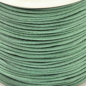 Puede incluir: Una bobina de cordón de algodón encerado verde. El cordón está enrollado firmemente alrededor de la bobina, creando una superficie lisa y uniforme.