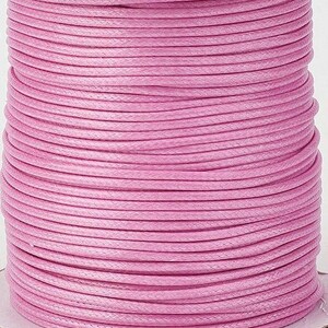 Könnte beinhalten: Eine Spule mit rosa gewachstem Baumwollgarn. Das Garn ist fest gewickelt und hat eine glatte, polierte Oberfläche.