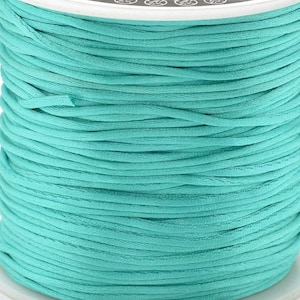 Può includere: Un rocchetto di cordoncino di cotone cerato di colore blu turchese. Il cordoncino è avvolto strettamente attorno al rocchetto.