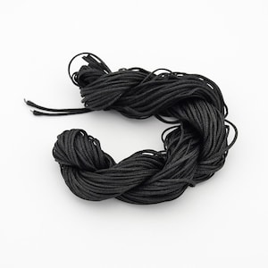 May include: A tightly wound bundle of black cord, likely nylon or similar material, against a white background. The cord is smooth and appears to be of a consistent thickness, suitable for various crafting or jewelry-making projects.