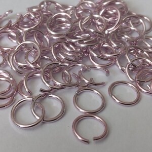 Könnte beinhalten: Ein großer Haufen kleiner, silberfarbener Sprungringe in hellrosa. Die Ringe sind alle offen und bereit für die Schmuckherstellung.