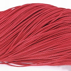 Puede incluir: Primer plano de un carrete de cordón rojo. El cordón está trenzado y tiene una superficie texturizada.