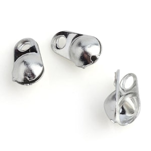 May include: Three silver-toned jingle bells with a loop for attaching to a project. The bells are small and have a shiny finish.