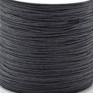 以下が含まれることがあります： 黒いワックス加工の綿糸の糸巻き。糸は糸巻きにしっかりと巻かれています。