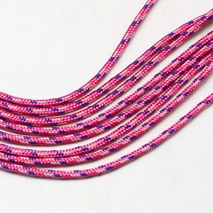 Könnte beinhalten: Nahaufnahme von mehreren rosa und lila gemusterten Kordeln. Die Kordeln sind eng gewebt mit einem sich wiederholenden Muster aus Rosa, Weiß und Lila. Die Kordeln sind leicht gebogen und parallel vor einem weißen Hintergrund angeordnet.