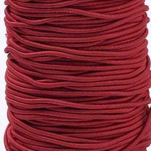 Könnte beinhalten: Eine Spule mit dunkelroter elastischer Kordel, die in mehreren horizontalen Schichten fest aufgewickelt ist. Die Kordel hat eine glatte, abgerundete Textur und eine durchgehend gleichmäßige, dunkelrote Farbe über die gesamte Spulenlänge.