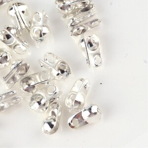 May include: Silver-toned metal bead caps with a loop on one end and a small ball on the other end. The bead caps are scattered on a white surface.