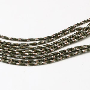 Könnte beinhalten: Nahaufnahme eines Bündels aus grünem, braunem und silbernem Tarnparacord. Das Paracord ist in einer geschwungenen Form angeordnet.