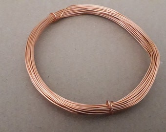 Puede incluir: Una bobina de alambre de cobre, enrollada en un círculo, sobre una superficie marrón.