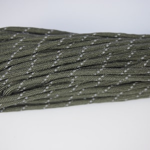 May include: A close-up of a green and white paracord rope. The rope is coiled and has a reflective thread woven into it.