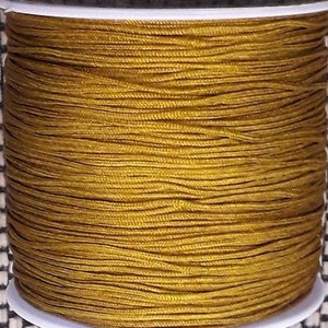 Könnte beinhalten: Eine Spule mit goldfarbenem gewachstem Garn. Das Garn ist fest um die Spule gewickelt.