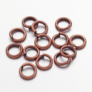 May include: A group of 15 copper jump rings, each with a diameter of approximately 5/16 inch. The rings are scattered on a white surface.