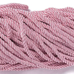 Peut inclure: Gros plan sur un paquet de corde torsadée. La corde est de couleur rose poudré avec des accents blancs, créant un motif rayé. La texture semble douce et souple, adaptée à divers projets d'artisanat.