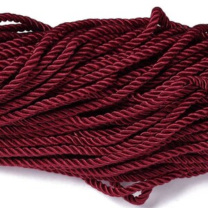 May include: A close-up of a spool of deep red twisted cord. The cord is made of a soft, silky material and has a subtle sheen.