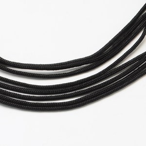 Könnte beinhalten: Nahaufnahme einer schwarzen Schnurkette mit mehreren Strängen. Die Kette besteht aus einer dicken, geflochtenen Schnur.
