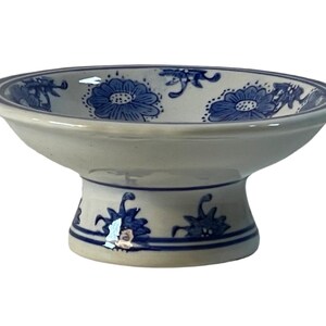 May include: A white ceramic pedestal bowl with a blue and white floral design. The bowl has a wide, shallow base and a raised center.