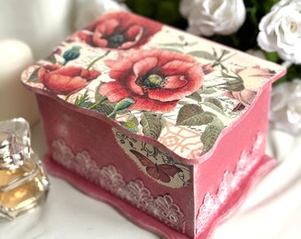 May include: A pink wooden box with a floral design featuring red poppies and green leaves. The box has a white lace trim and a butterfly design on the side.
