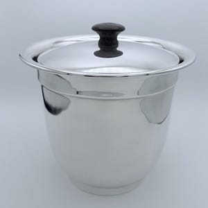 May include: A shiny, silver ice bucket with a lid and a black handle. The bucket has a rounded shape with a slightly flared rim. The lid sits flush on top, and the black handle provides a contrasting accent.
