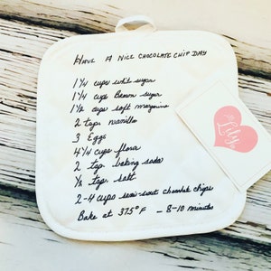 May include: White pot holder with a handwritten chocolate chip cookie recipe. The recipe includes ingredients such as white sugar, brown sugar, soft margarine, vanilla, eggs, flour, baking soda, salt, and semi-sweet chocolate chips. The recipe also includes baking instructions to bake at 375 degrees Fahrenheit for 8-10 minutes.