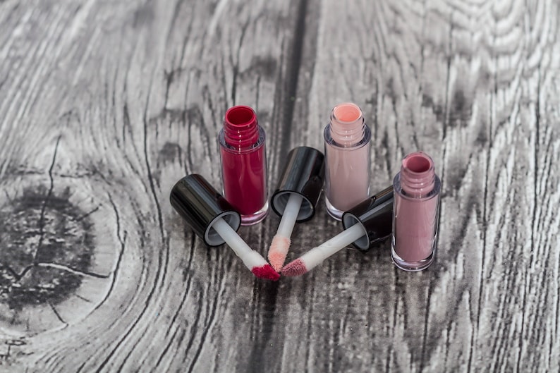 May include: Four clear lip gloss tubes with black caps and doe-foot applicators. The lip glosses are in shades of pink, red, and nude.