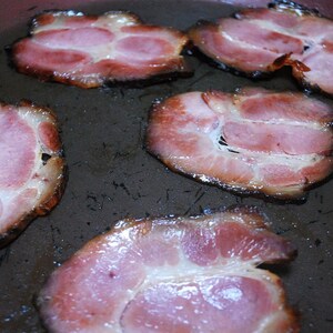 May include: Close-up of five rashers of cooked bacon in a frying pan. The bacon is crispy and has a light brown colour.