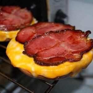May include: Two toasted English muffins topped with melted cheese and crispy bacon.