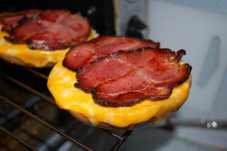 May include: Two toasted English muffins topped with melted cheese and crispy bacon.