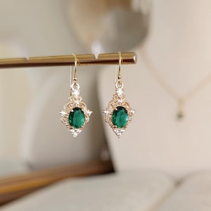 May include: A pair of gold dangle earrings with green oval-shaped gemstones surrounded by smaller clear gemstones.