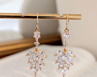 May include: Gold dangle earrings with a cluster of clear cubic zirconia stones in a leaf shape.