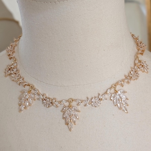 May include: A gold necklace with a delicate design featuring clear crystal leaves. The necklace is on a white mannequin bust.