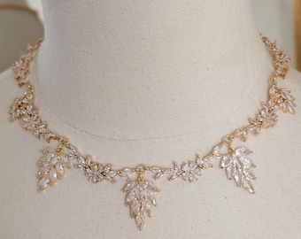 May include: A gold necklace with a delicate design featuring clear crystal leaves. The necklace is on a white mannequin bust.